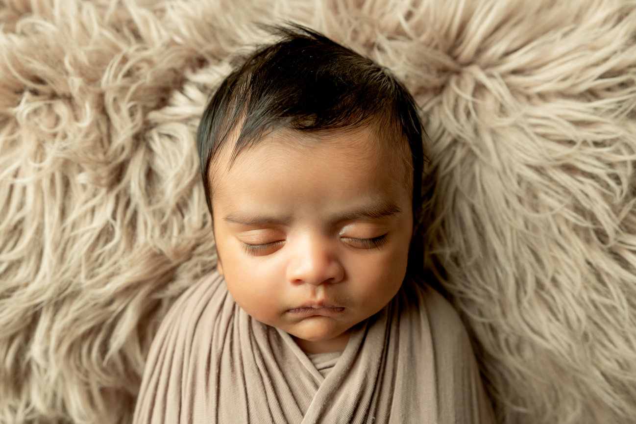 Sleeping baby wrapped in a soft blanket, lying on a fluffy rug.
