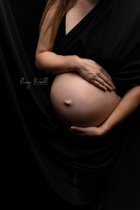 Pregnant woman holding her belly in a dark studio portrait at the studio of Angi Randall Photography located in Augusta, Wisconsin.