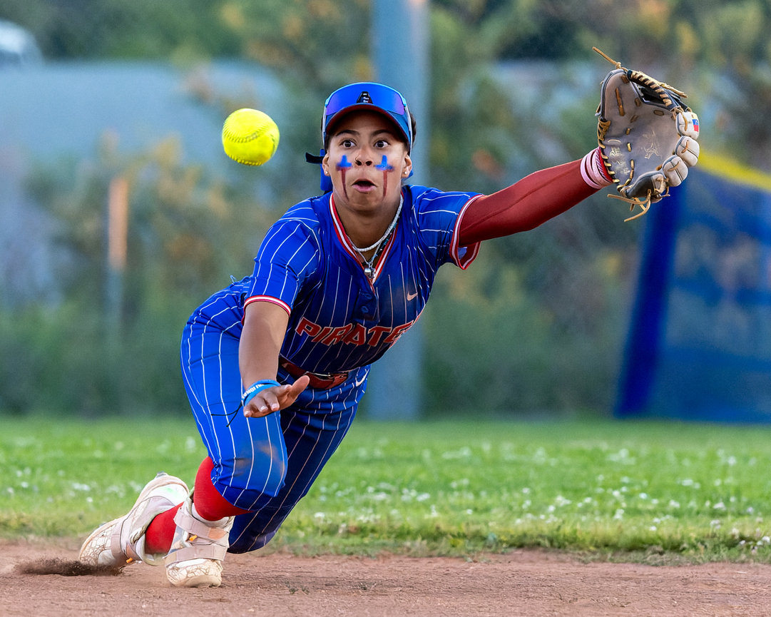 Baseball infielder diving to field a ground ball on the grass.