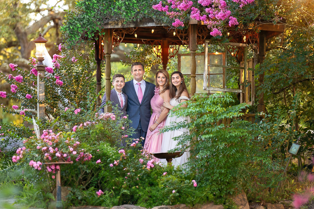 Couple posing in a lush garden with blooming flowers and a gazebo