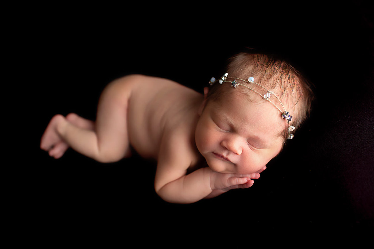 Newborn baby girl sleeping in side laying pose on black backdrop during newborn photo session with Kansas City photographer Dreamworks Photography