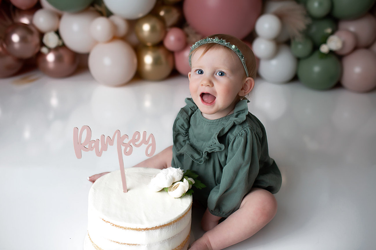 baby girl smiling with birthday cake during first birthday cake smash photoshoot with cake smash photographer Dreamworks Photography in Kansas City