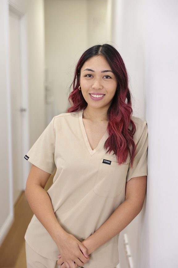 Smiling woman in beige scrubs with pink hair standing in a hallway. Business content photos melb
