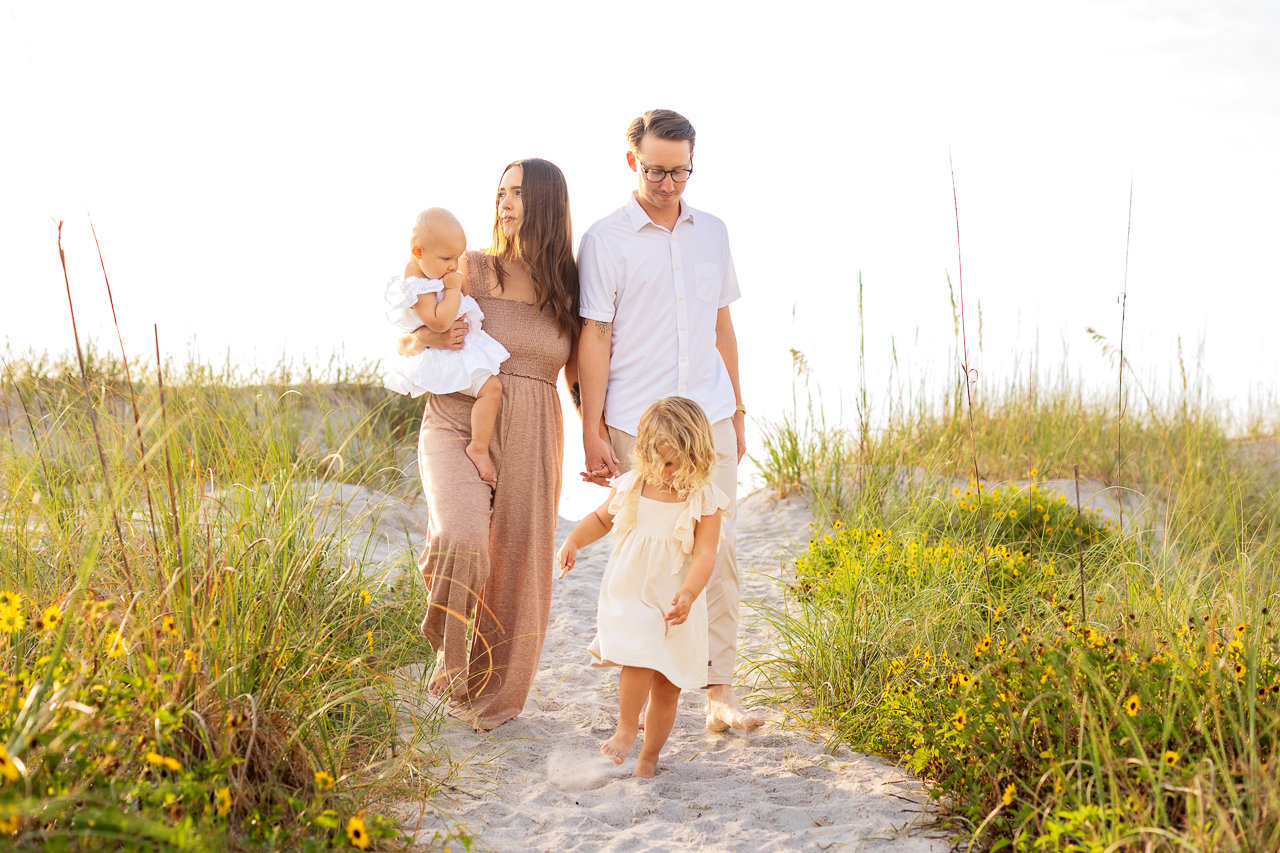 A joyful family moment captured by a skilled family photographer in Jacksonville, Florida—parents holding their toddler, smiling and basking in the warmth of each other's company against a backdrop of serene sand dunes