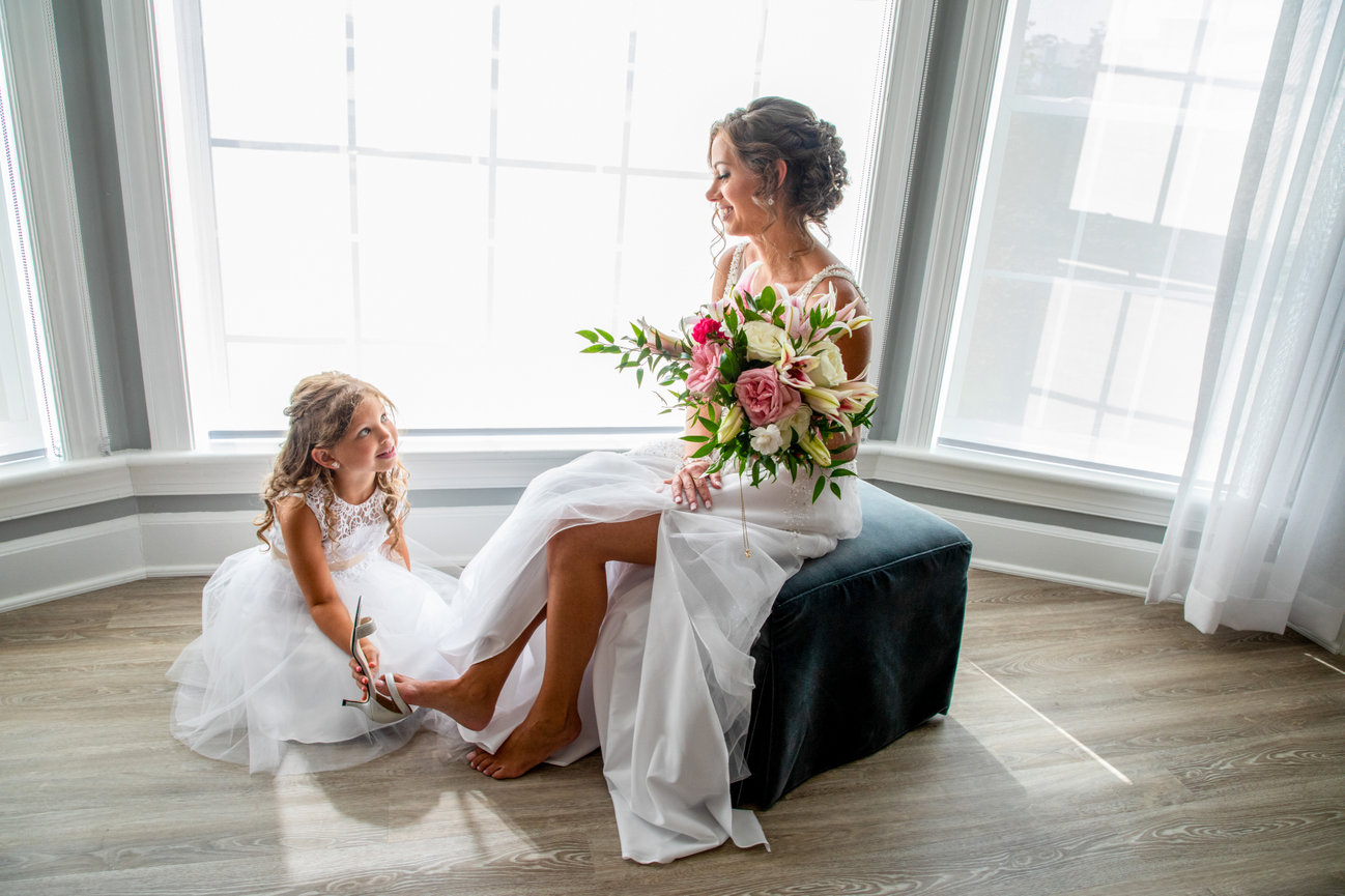 Bride and her bridesmaid with bouquets beside bright windows before the ceremony