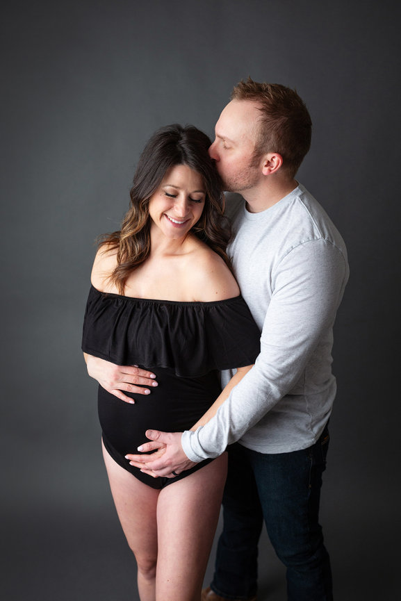 Couple embracing; man kisses woman's head while holding her baby bump.