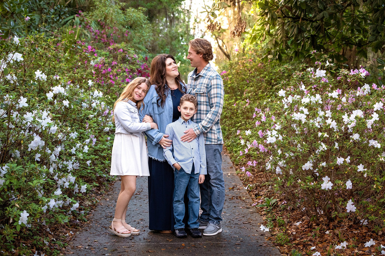 A joyful family photoshoot in St. Augustine, Florida: parents lovingly gaze at their baby, who wears an adorable bow tie, as they embrace in a sunlit outdoor setting.