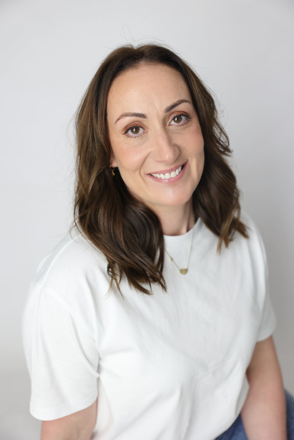 Smiling woman with brown hair wearing a white shirt against a light gray background. authentic photos for my business and website
