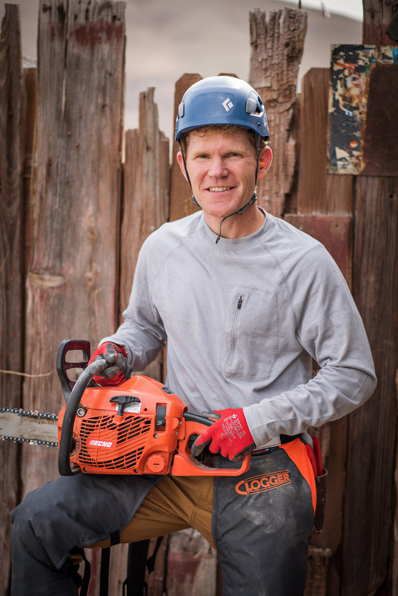 Man with a chainsaw posing in front of a wood fence for an advertising photo shoot for his tree trimming business in Utah.