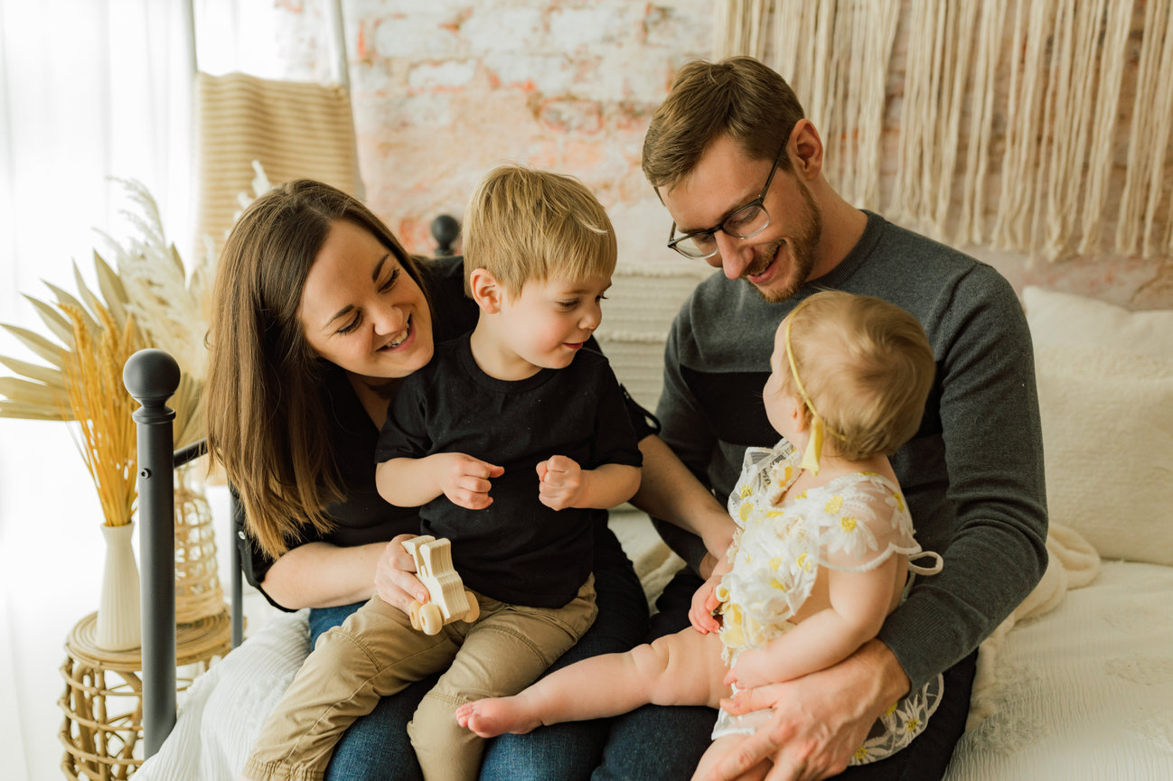 Parents cuddling both siblings on vintage bed setup in natural light studio