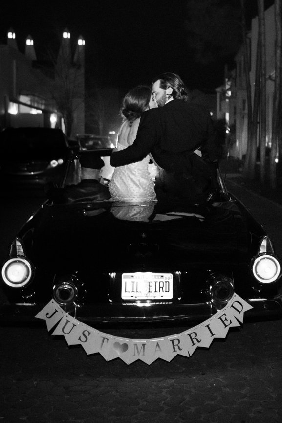 Black and white image of bride and groom kissing on the back of a convertible in Alys Beach, Florida. Destination wedding photography by Heather Durham.