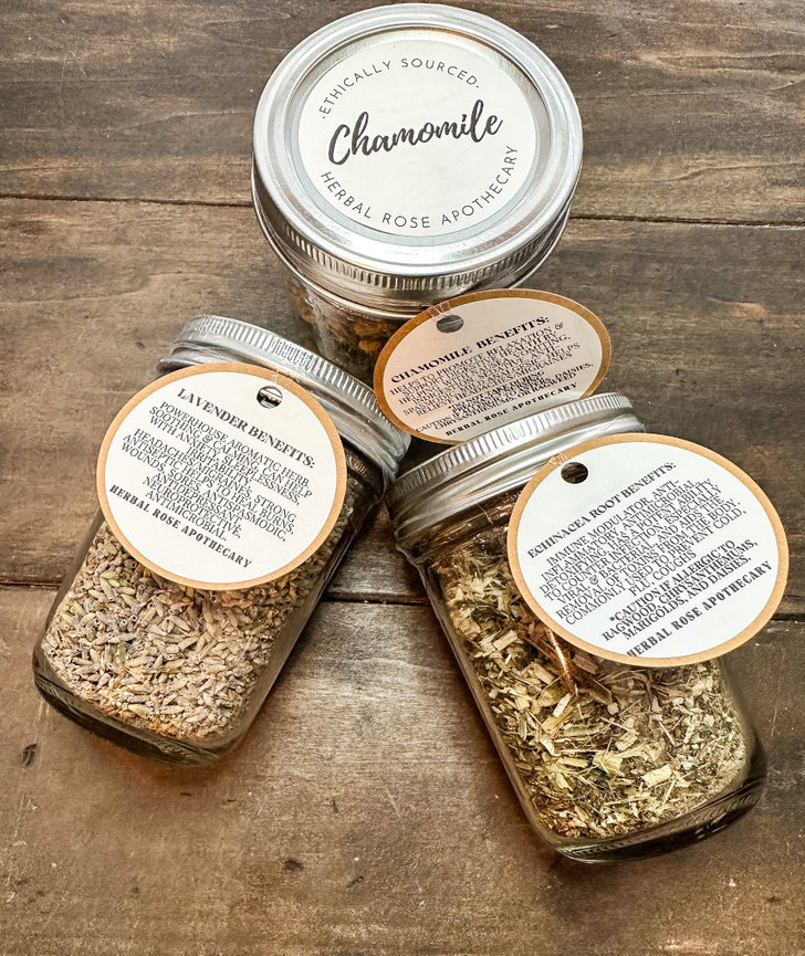 Jars of dried herbs labeled chamomile, lavender, and echinacea on a wooden surface.