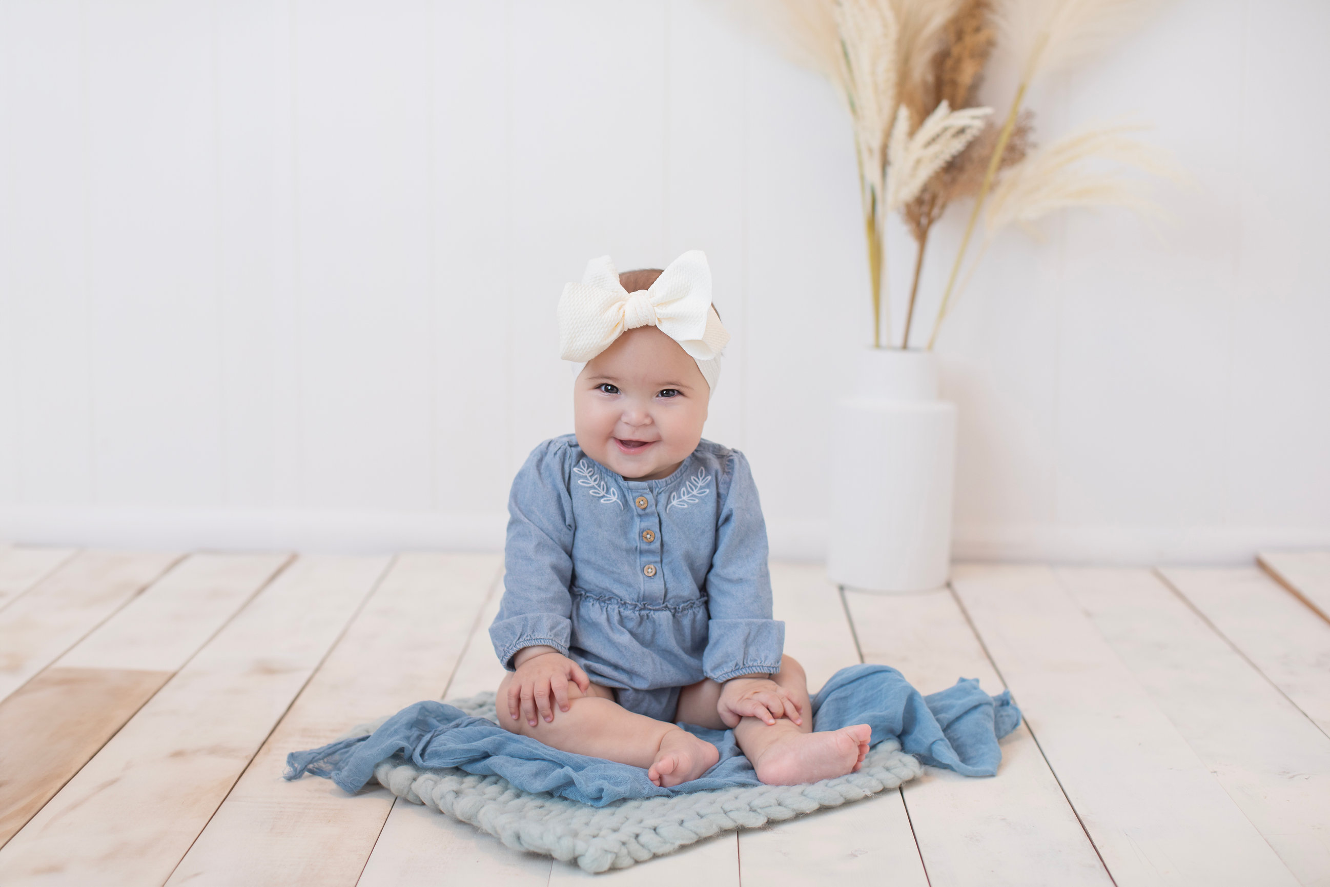 Smiling baby in a denim outfit sitting on a woven rug