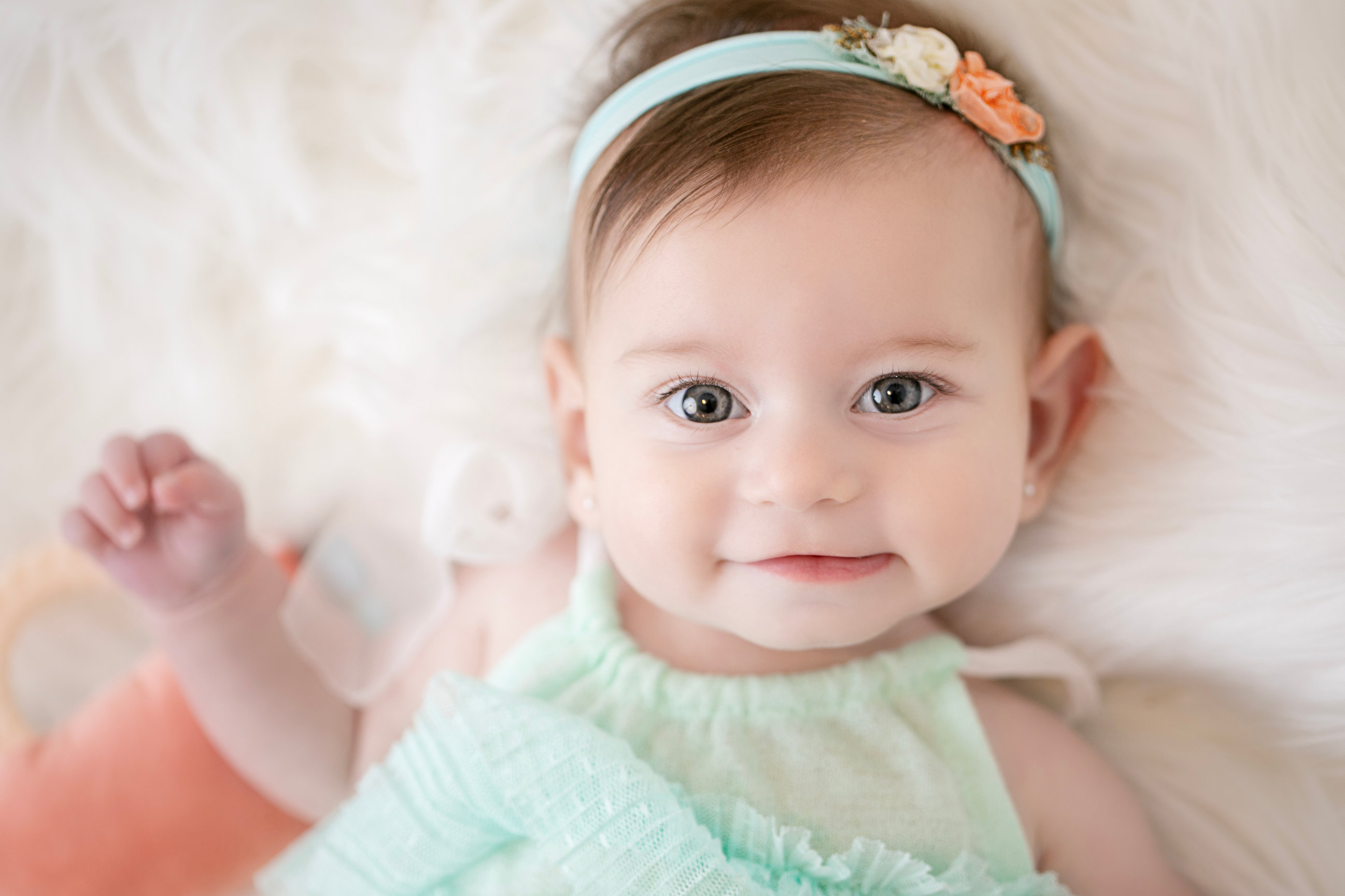 Baby in a mint dress smiling on a cream blanket