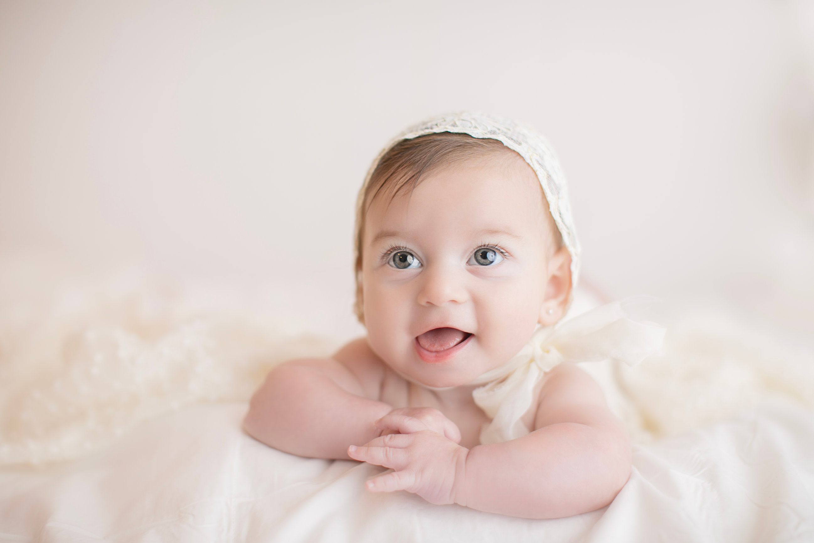 Baby smiling during tummy time on a cream blanket