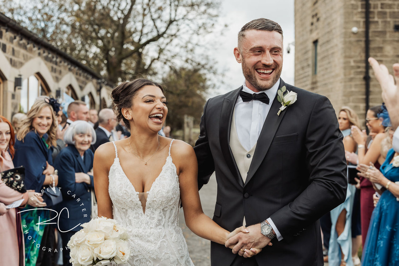 Bride and groom smiling while walking past cheering guests at an outdoor wedding ceremony.