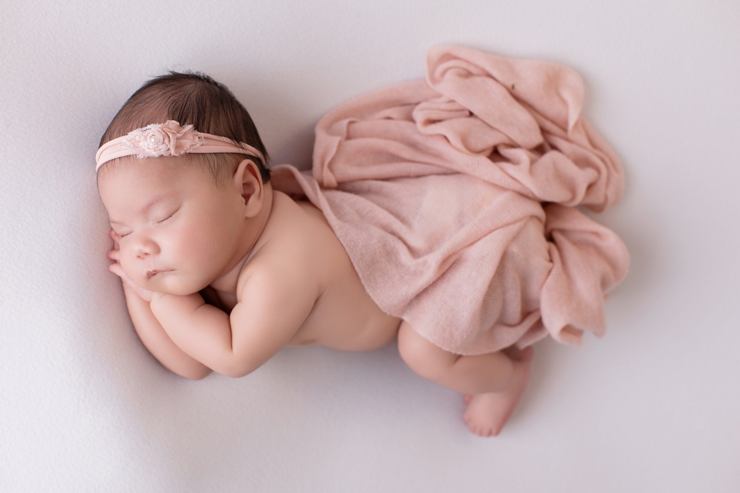 Newborn girl asleep in a soft blush wrap on a white backdrop