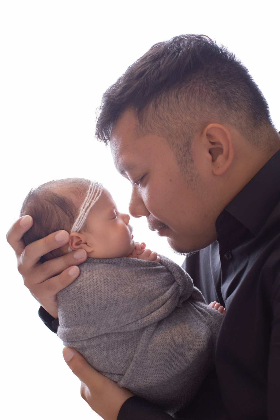 Father kissing his newborn daughter wrapped in a soft grey wrap