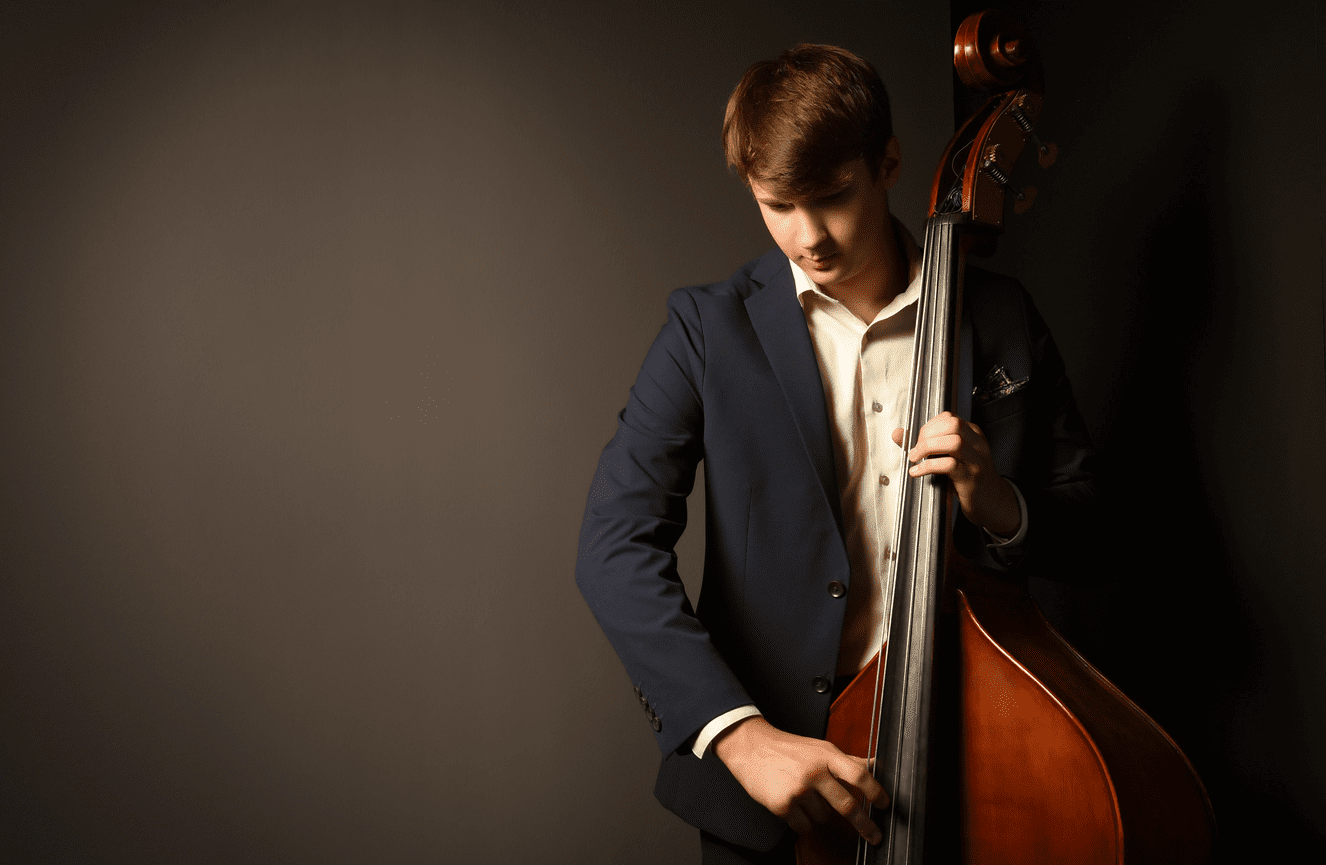 Leo, wearing a suit jacket, is playing his base during his high school senior portrait session at Kliks Photography.