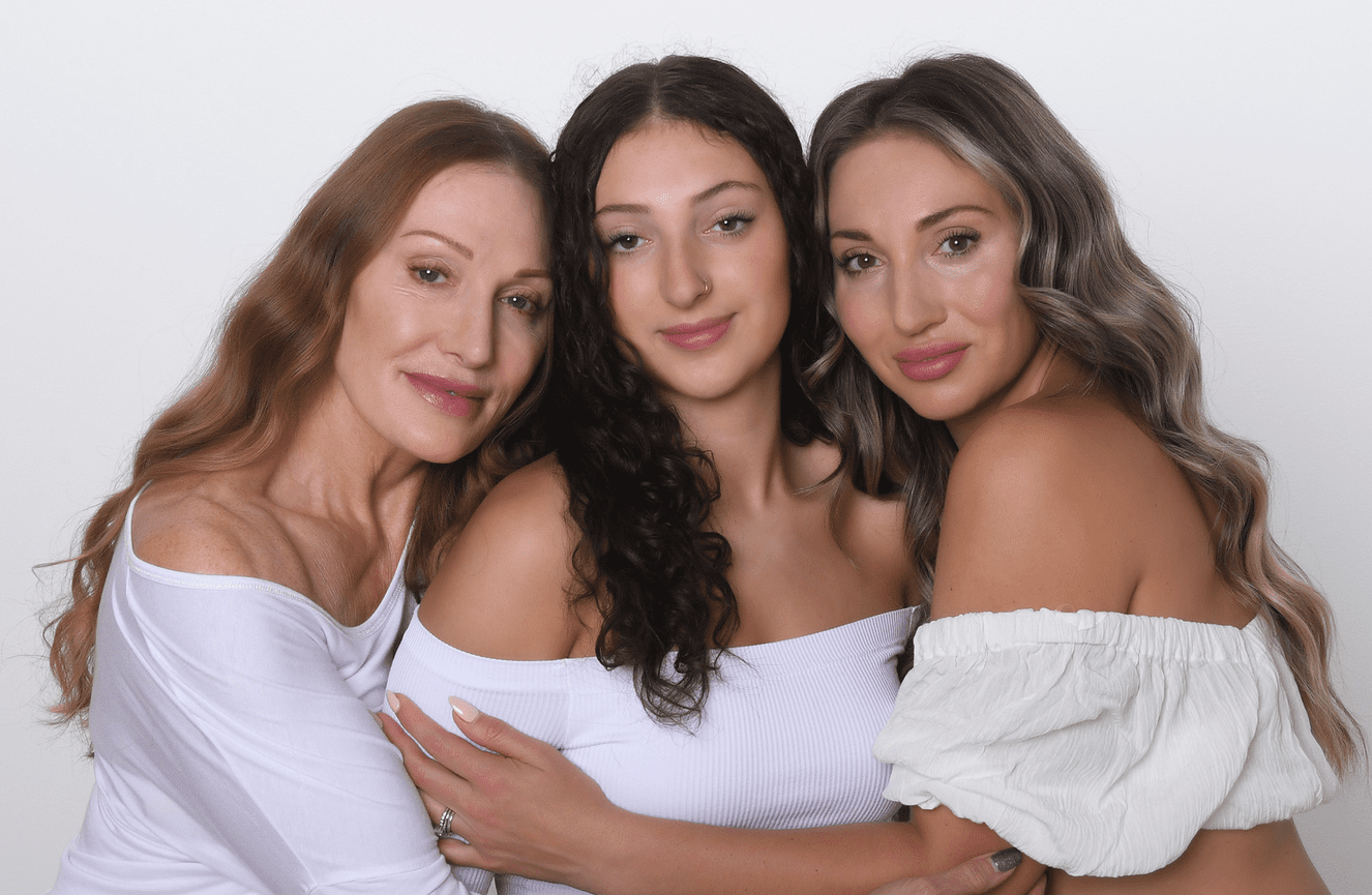 Three generations of a grandmother, daughter, and granddaughter sitting closely wearing white off the shoulder blouses.