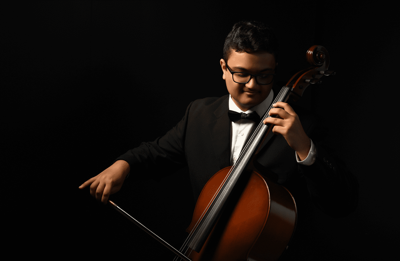 A young man in a tuxedo plays his cello.