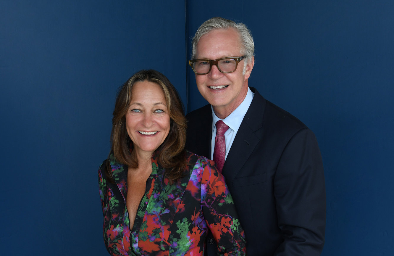 A wife wearing a red, navy, and green floral dress with her husband in a dark blue suit and matching red tie at Kliks Photography.