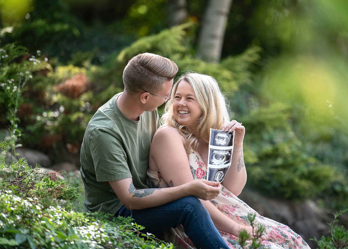A couple sitting outdoors, smiling, and holding an ultrasound image.