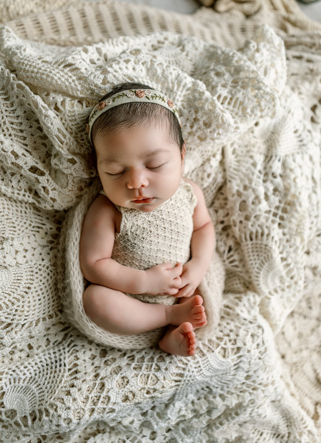 Newborn baby sleeping peacefully on a soft, textured cream blanket.