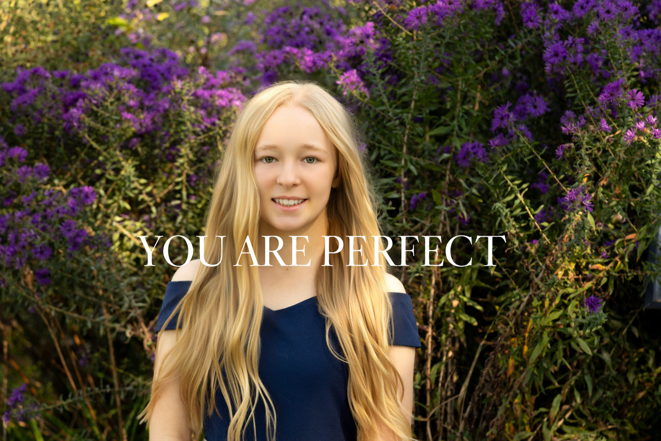 A person with long hair standing in front of purple flowers, with the text You Are Perfect overlaid.