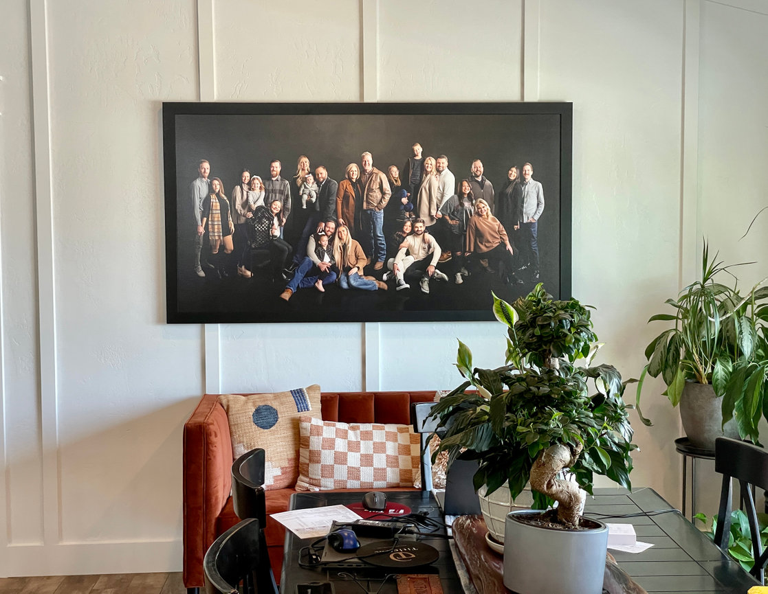 Framed group portrait hanging above a chair with plants in a bright home interior