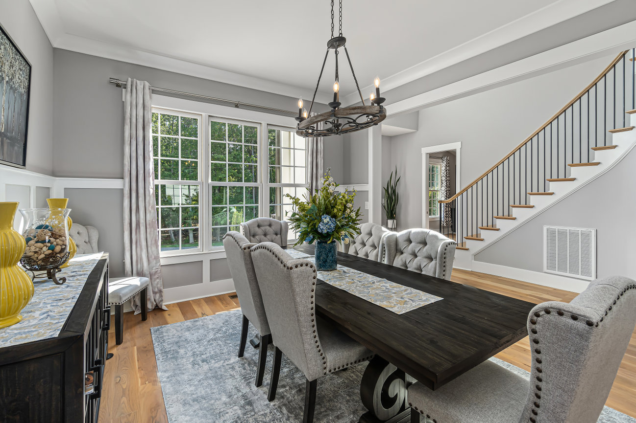 Elegant dining room with dark wood table, gray chairs, large windows, and a staircase nearby