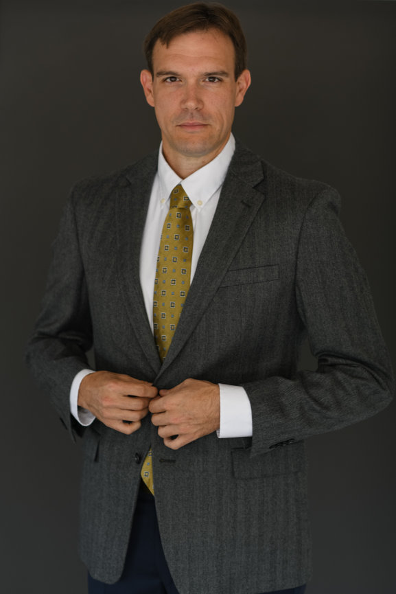 Man in a formal gray suit and patterned tie, adjusting his jacket against a dark background for updated branding portraits in Columbus Ohio.