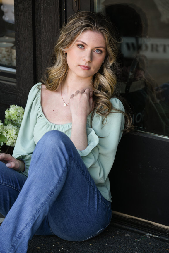 Teen girl sitting on the ground next to a black wall, wearing a soft green shirt during her senior photo session