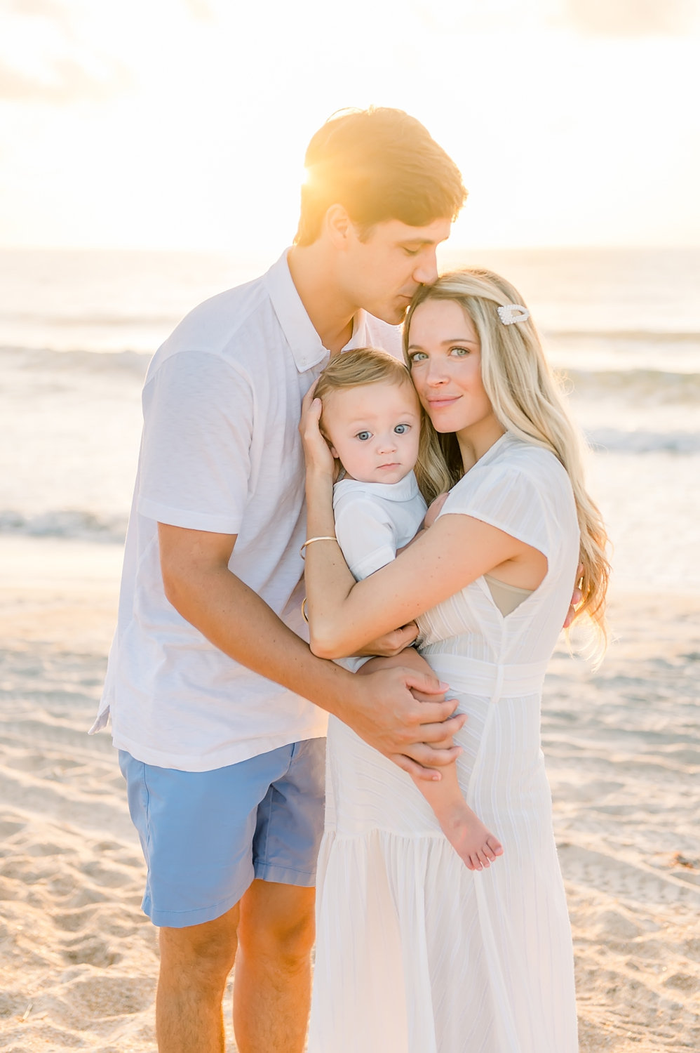 husband kissing wife's forehead, family of three, Florida family coastal portrait session