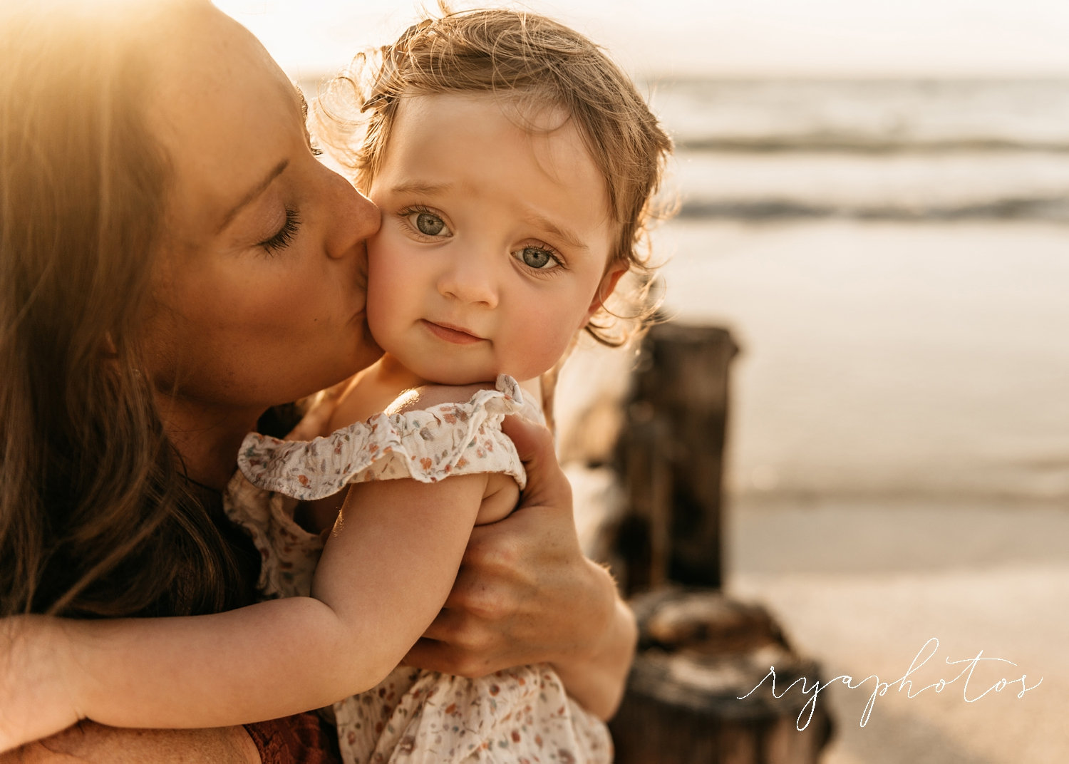 mother kissing baby daughter, baby girl with big blue eyes, sun flare, Rya Duncklee