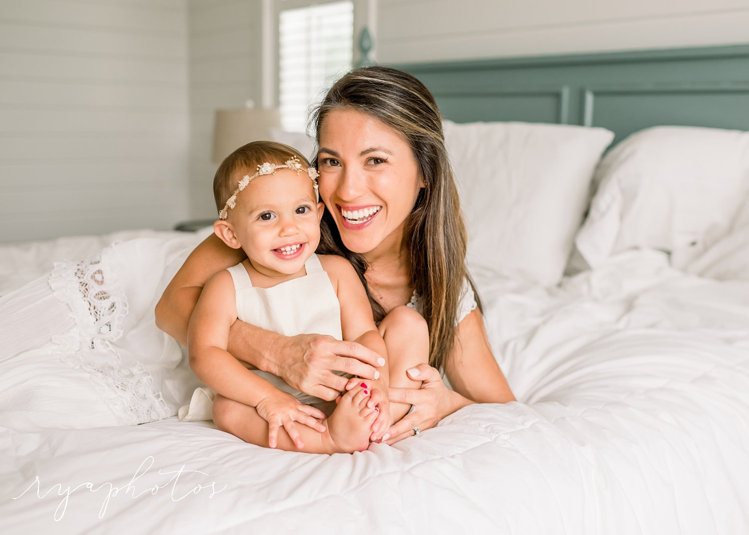 mother and baby daughter smiling at the camera, white bed, Rya Duncklee Photography