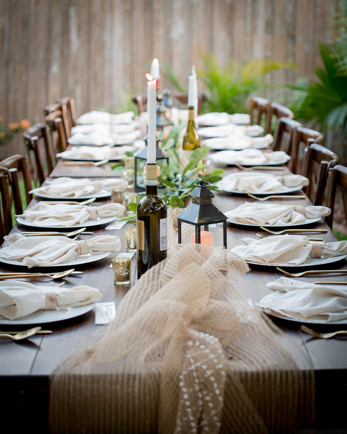 Elegant outdoor dining setup with a long wooden table, candles, and decorative elements.