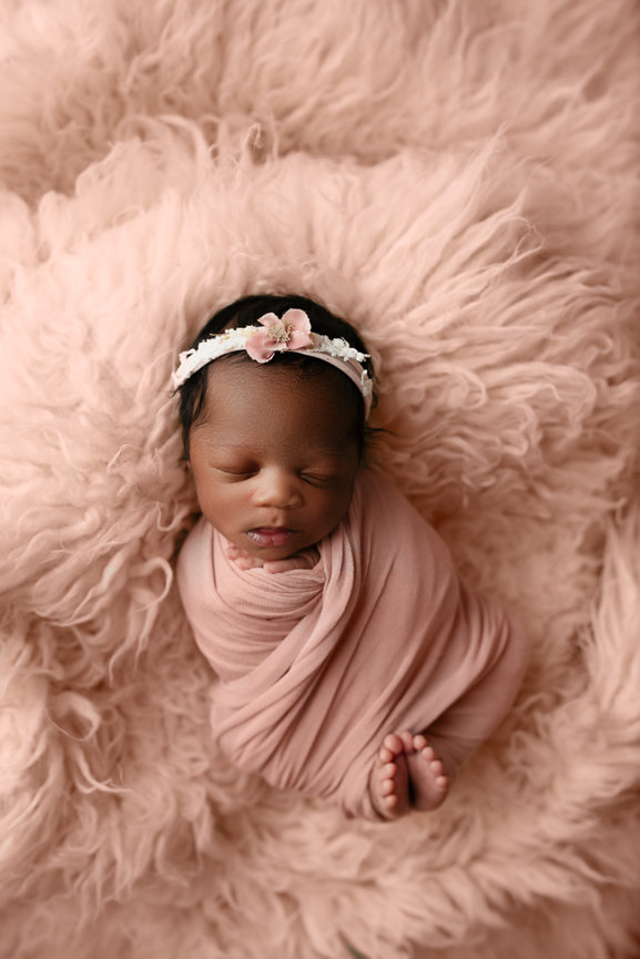 newborn baby girl swaddled in a pink wrap and a pink headband on